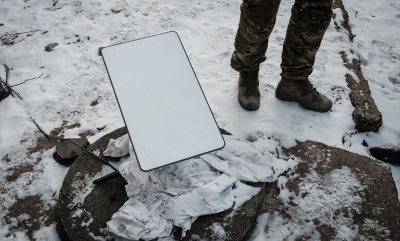 Starlink satellite dish set up in snowy conditions, near a person in camouflage.