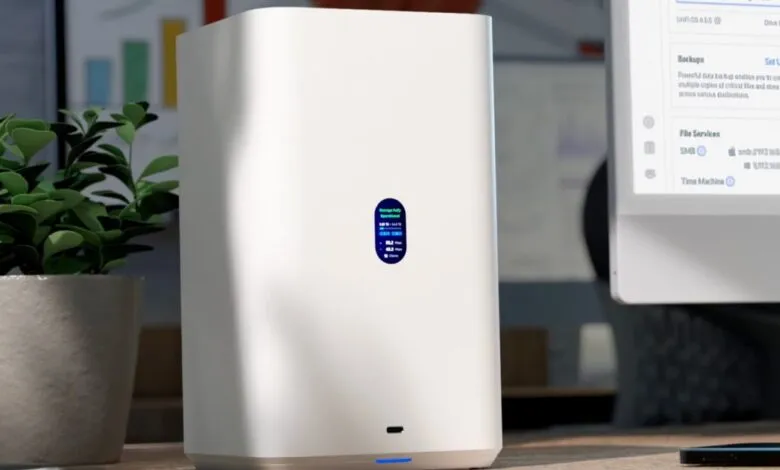 White network storage device on a desk, next to a plant and computer showing file backups and Time Machine.