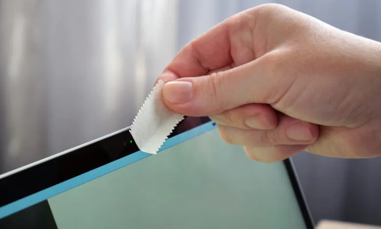 Hand placing a webcam cover over a laptop camera for privacy.