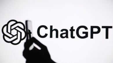 Silhouette of a hand holding a smartphone, capturing the ChatGPT logo on a bright screen.