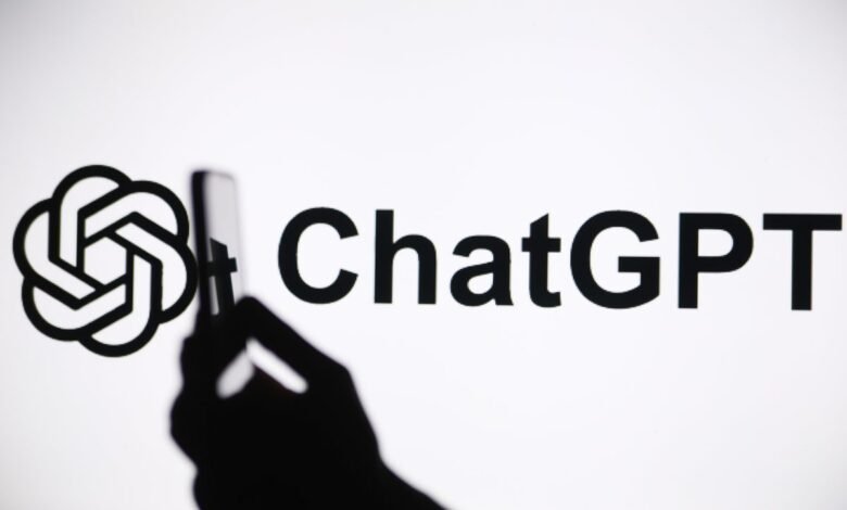 Silhouette of a hand holding a smartphone, capturing the ChatGPT logo on a bright screen.