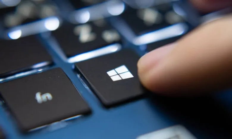 Close-up of a finger pressing the Windows key on a black keyboard.