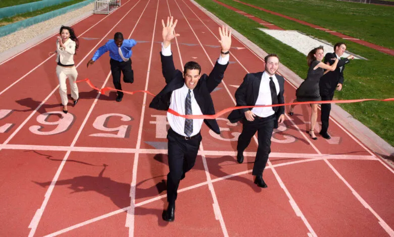 Businesspeople crossing finish line, celebrating victory. Red track, red ribbon.