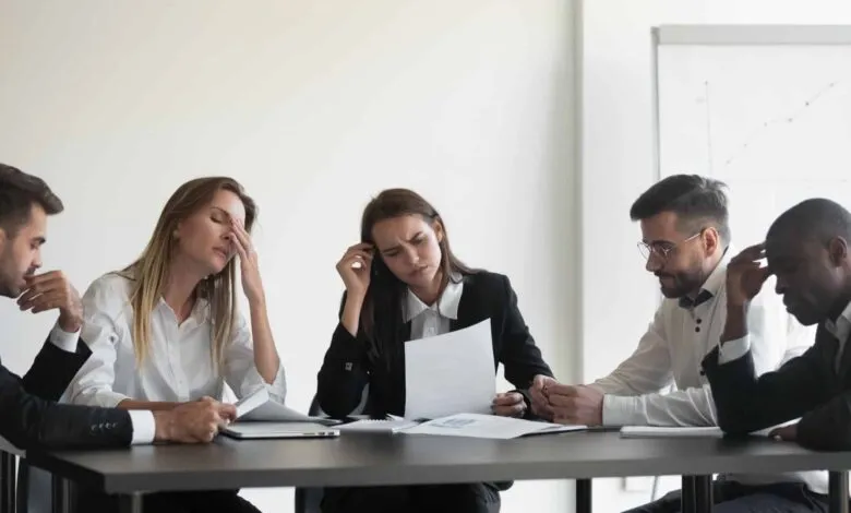 Stressed business team reviewing documents at a meeting, showing frustration and concern.