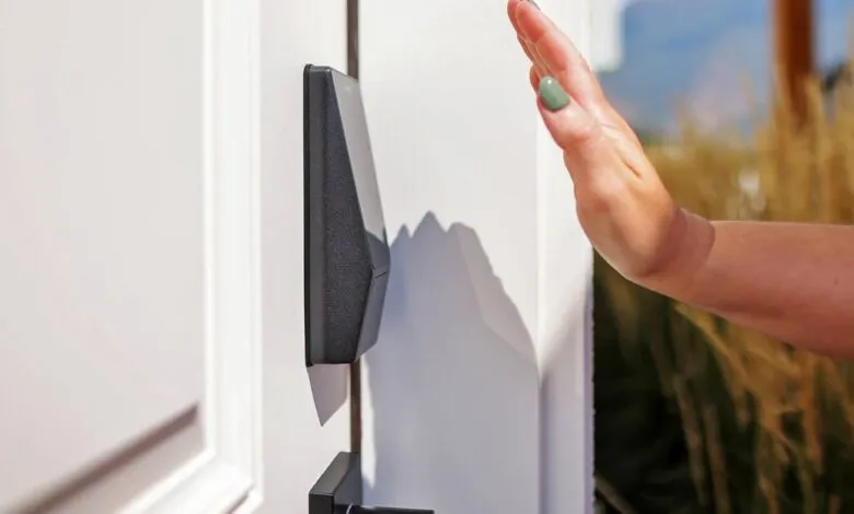 Hand approaching a sleek, black smart lock mounted on a white door. Modern home security.