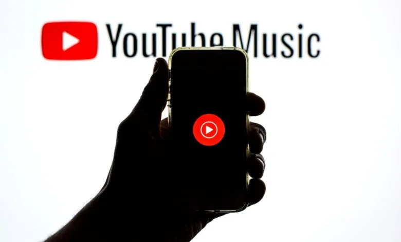 Silhouette of a hand holding a smartphone displaying the YouTube Music logo.