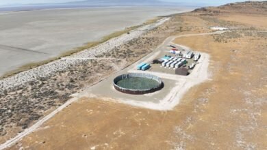 Aerial view of an industrial facility with a large circular pond and modular buildings near a dry lakebed.