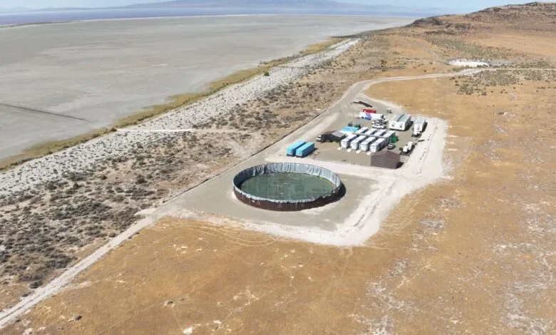 Aerial view of an industrial facility with a large circular pond and modular buildings near a dry lakebed.