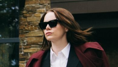 Woman with auburn hair wearing sunglasses and a maroon coat over a white shirt.