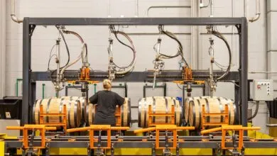 Worker overseeing automated barrel filling process in a distillery