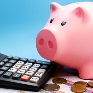 Pink piggy bank next to a calculator and coins on a financial chart.