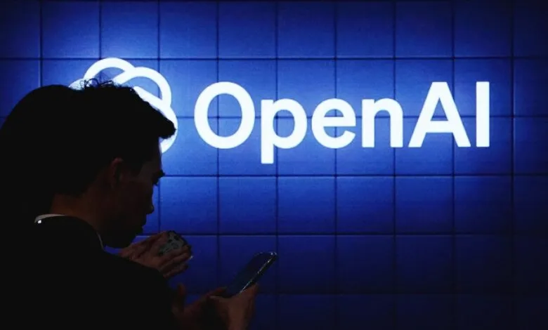 Silhouettes of people looking at the glowing white OpenAI logo on a blue tiled screen.