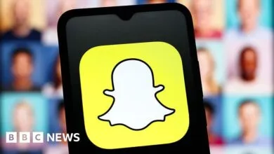 Close-up of the Snapchat logo on a smartphone screen, with blurred faces in the background.