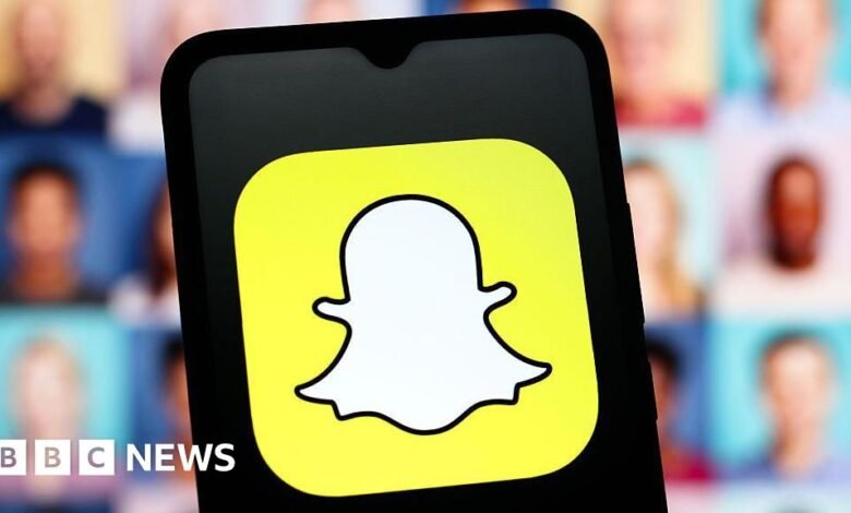 Close-up of the Snapchat logo on a smartphone screen, with blurred faces in the background.