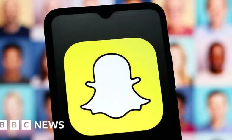 Close-up of the Snapchat logo on a smartphone screen, with blurred faces in the background.