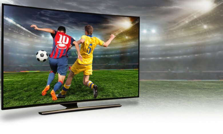 Soccer players competing on a field displayed on a large television screen.