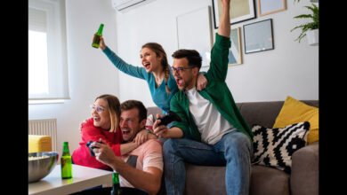 Four friends excitedly playing video games and celebrating a win, holding controllers and drinks.