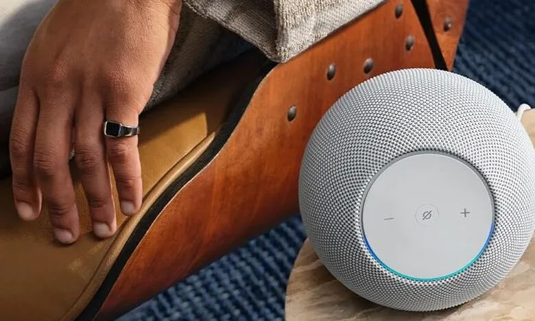 Close-up of a hand with a ring resting on a leather chair next to a white smart speaker.