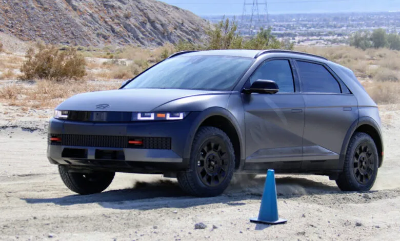 Matte gray Hyundai Ioniq 5 XRT driving on a dirt road with a blue cone.