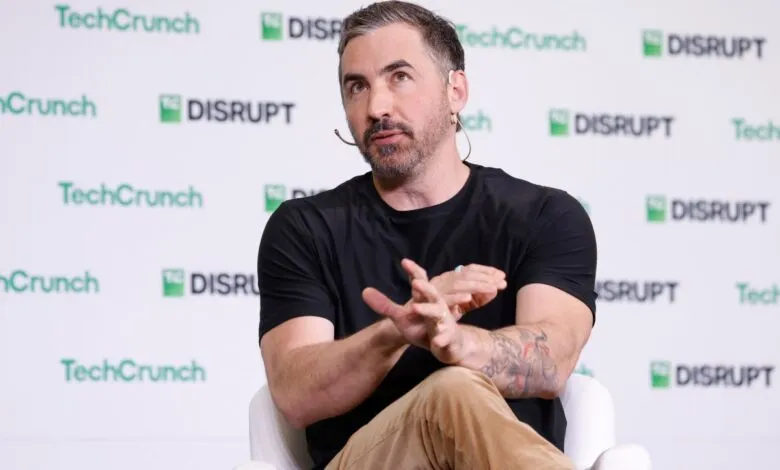 Man with beard and tattoos speaking on stage at TechCrunch Disrupt event.