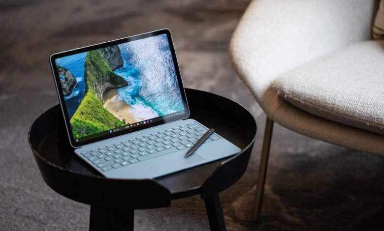 A light blue Microsoft Surface Pro laptop with a stylus rests on a black side table.