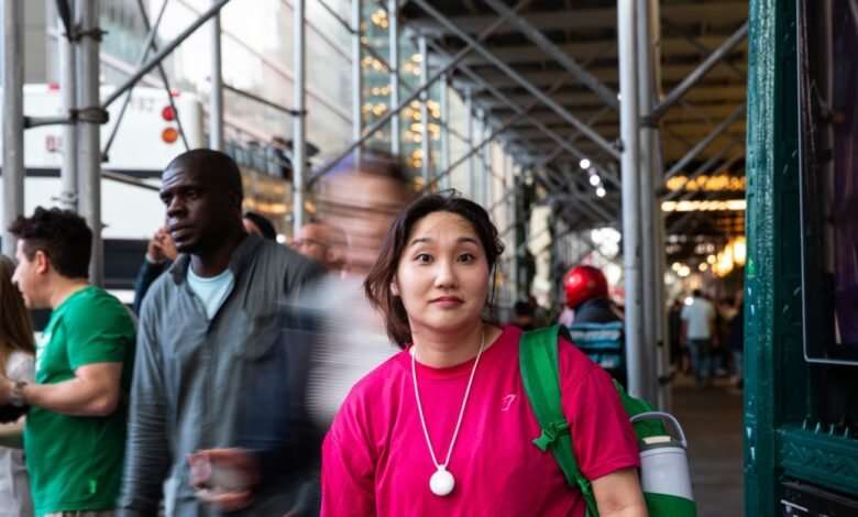 A young woman in a pink shirt looks at the camera on a busy city street.