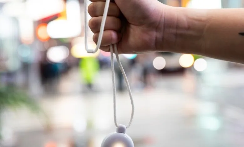Close-up of a hand holding a white lanyard with a small white pendant, blurred city lights in background.