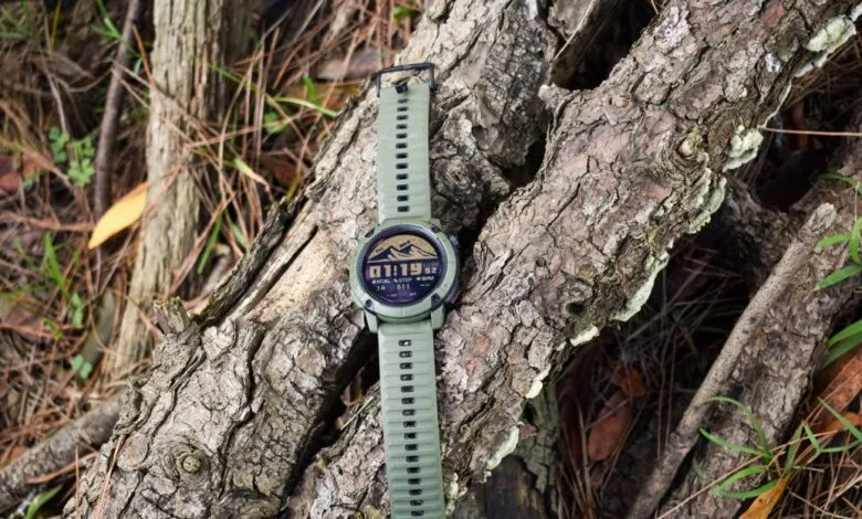 Green Coros Nomad smartwatch resting on a textured tree branch outdoors.