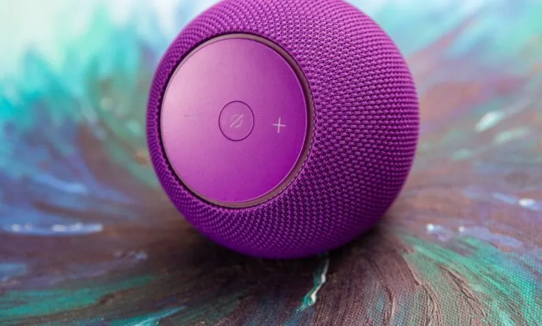 Close-up of a purple smart speaker with volume controls on a textured surface.