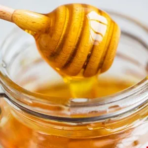 Wooden honey dipper dripping golden honey into a glass jar.