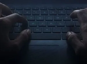 Close-up of hands typing on a laptop keyboard in low light.