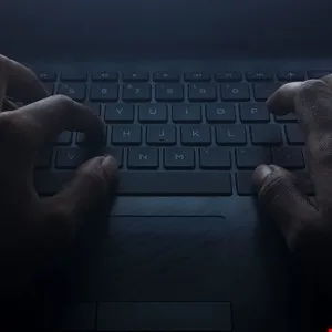 Close-up of hands typing on a laptop keyboard in low light.
