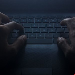 Close-up of hands typing on a laptop keyboard in low light.