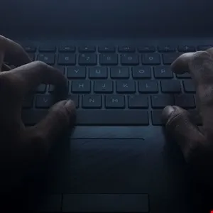Close-up of hands typing on a laptop keyboard in low light.
