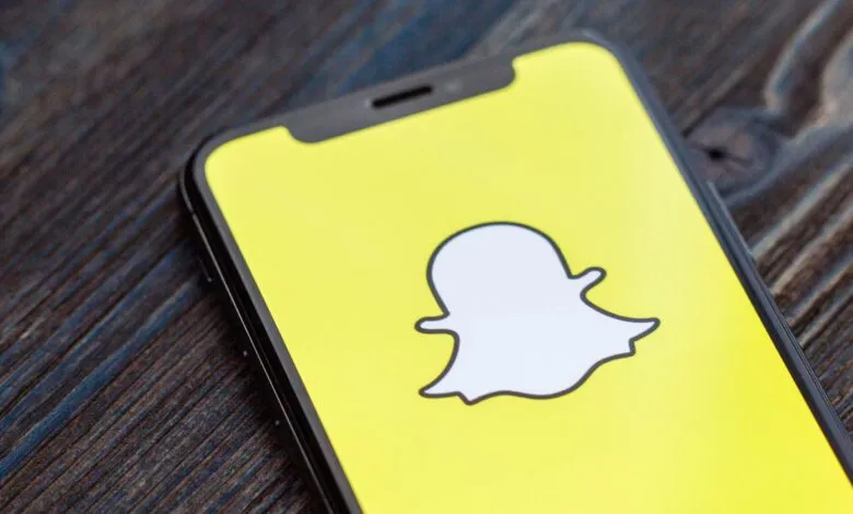Close-up of a smartphone displaying the Snapchat logo on a bright yellow screen.