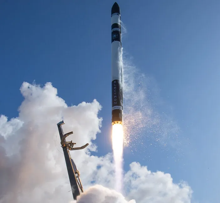 Rocket launch with bright flames and smoke against a blue sky with clouds.
