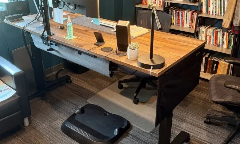 Modern office desk with dual monitors, standing desk converter, and ergonomic chair.