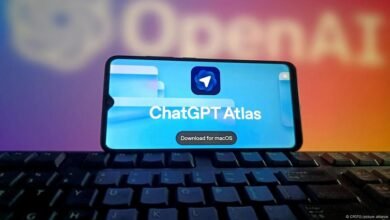 Smartphone displaying ChatGPT Atlas app with download button for macOS, placed on a keyboard.