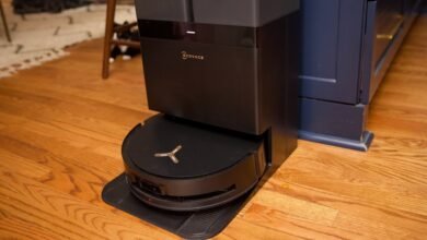Black Ecovacs Deebot robot vacuum docked on its charging station on a hardwood floor.