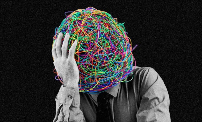 Person with head covered in tangled colorful wires, hand on forehead, black background.