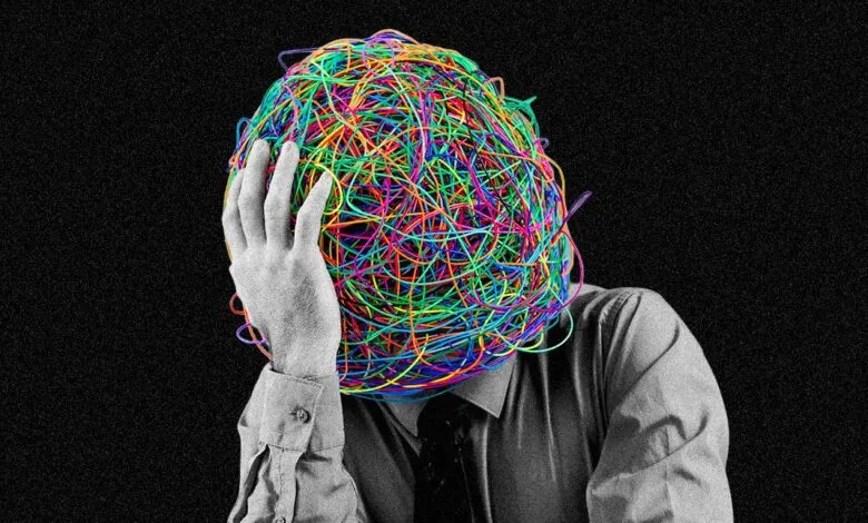 Person with head covered in tangled colorful wires, hand on forehead, black background.