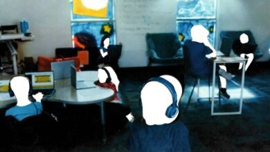 People wearing headphones work on laptops in a brightly lit room with colorful window art.