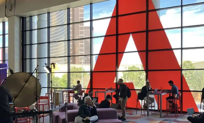 People working and networking in a modern space with a large red Adobe logo on the window.