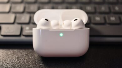 White Apple AirPods Pro earbuds in their charging case with a green indicator light.