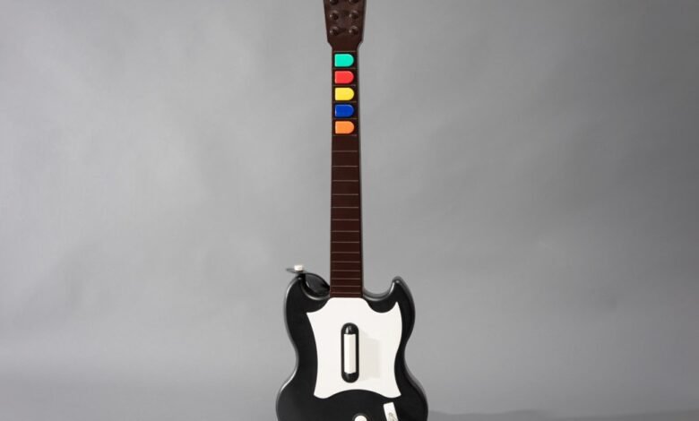 A black and white video game guitar controller with colored buttons on the fretboard.