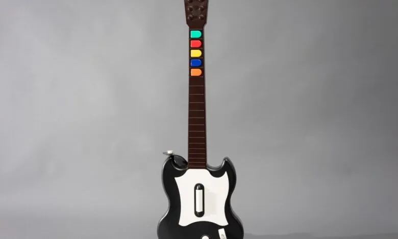 A black and white video game guitar controller with colored buttons on the fretboard.