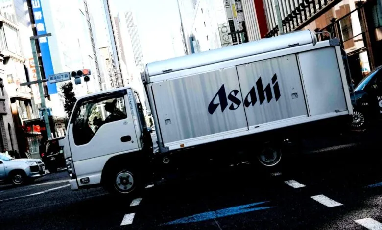 White Asahi delivery truck driving on a city street with tall buildings.