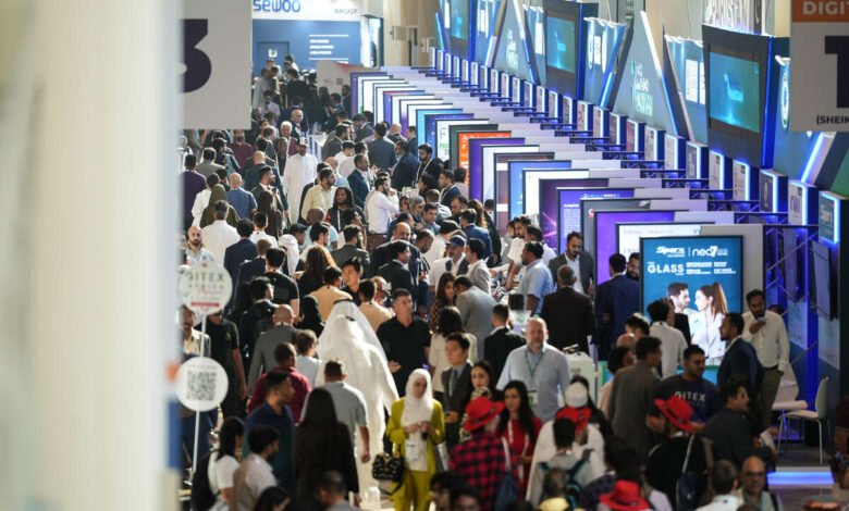Crowd of people attending a busy technology exhibition with booths and displays.