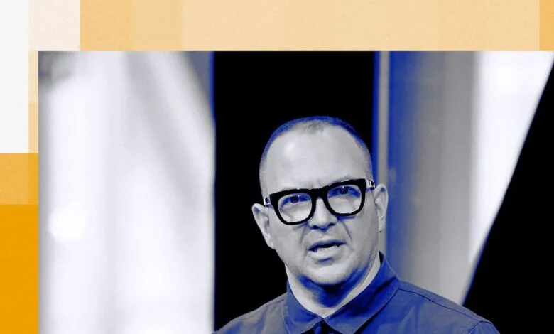 Close-up of a bald man with glasses speaking, with abstract orange and white geometric shapes in the background.