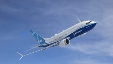 A white and blue Boeing 737 MAX airplane in flight against a clear blue sky.
